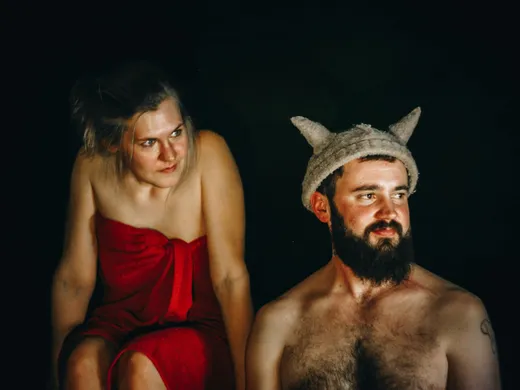 Vīrietis un sieviete pirts cepurēs un sarkanos dvieļos sēž uz pirts lāvas